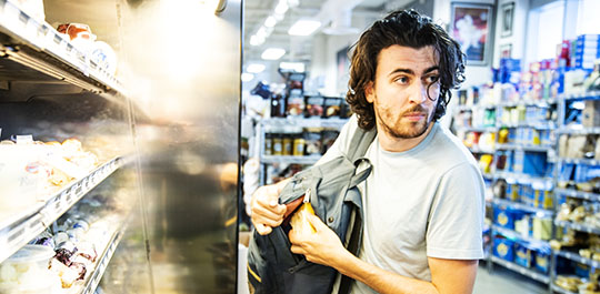 A male shoplifter stealing some expensive gourmet cheese in a specialty supermarket